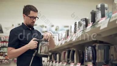 一个留胡子的男人正在五金店的大厅里检查玻璃电水壶
